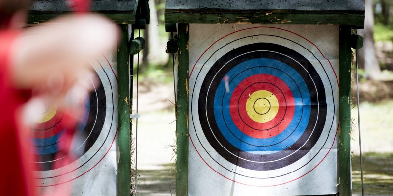 A selective focus shot of a target with a blurred person using bow and arrow